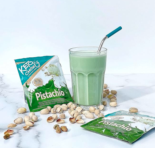 Keto Chow Pistachio flavor packet next to a finished pistachio shake with a glass straw and shelled pistachios