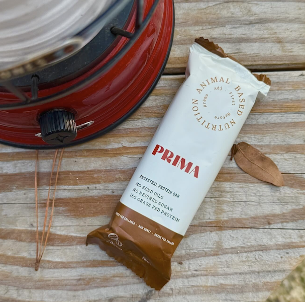Prima ancestral protein bar on a wooden table next to a camping lantern, representing the Prima Protein Bars Review