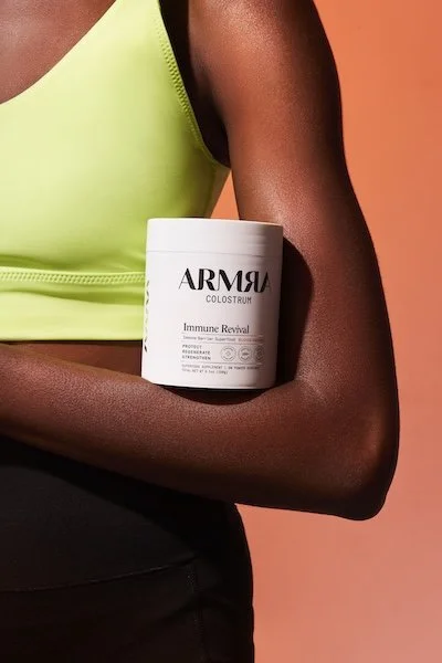 ARMRA Colostrum Immune Revival container resting on woman’s arm, highlighting digestive and immune support benefits