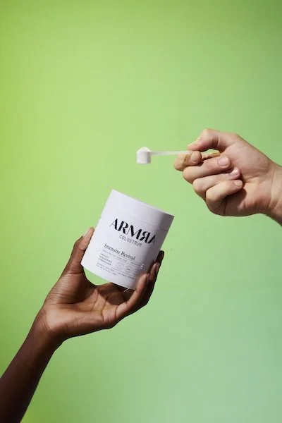 Hands holding ARMRA Colostrum Immune Revival container with scoop of powder, highlighting immune and gut health support