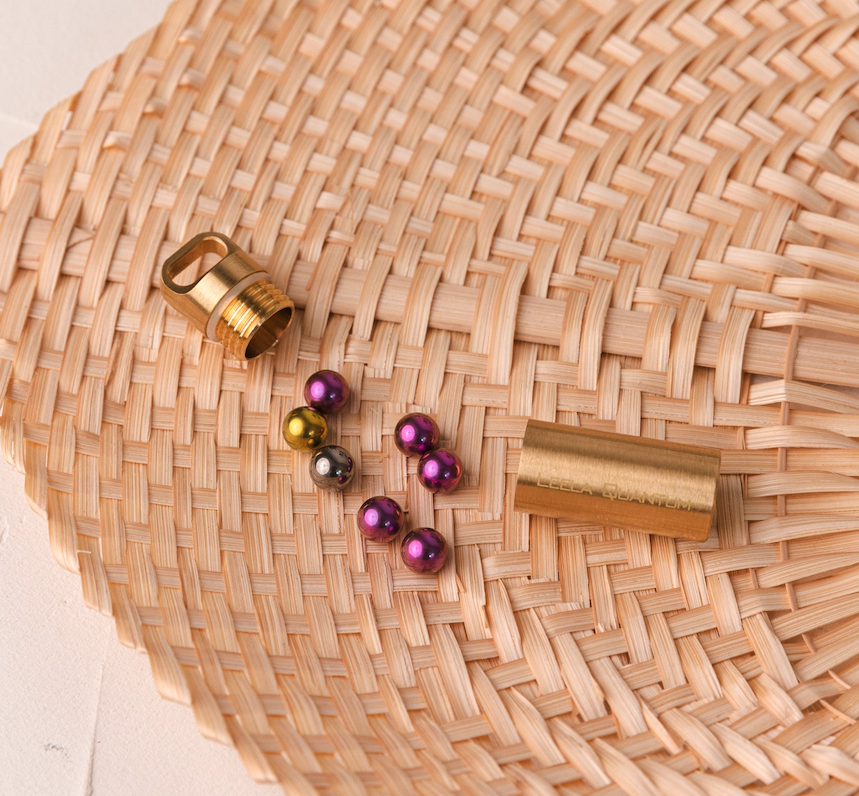 A Leela Quantum capsule unscrewed on a woven mat with its cap, body and loose titanium spheres