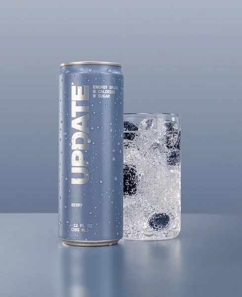 Update Energy Berry flavor energy drink can beside a glass of sparkling ice water, caffeine-free paraxanthine formula for smooth focus without jitters.
