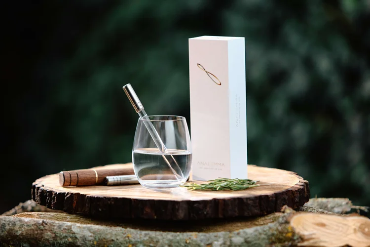 Analemma wand in a glass of water beside its box on a wooden slab outdoors