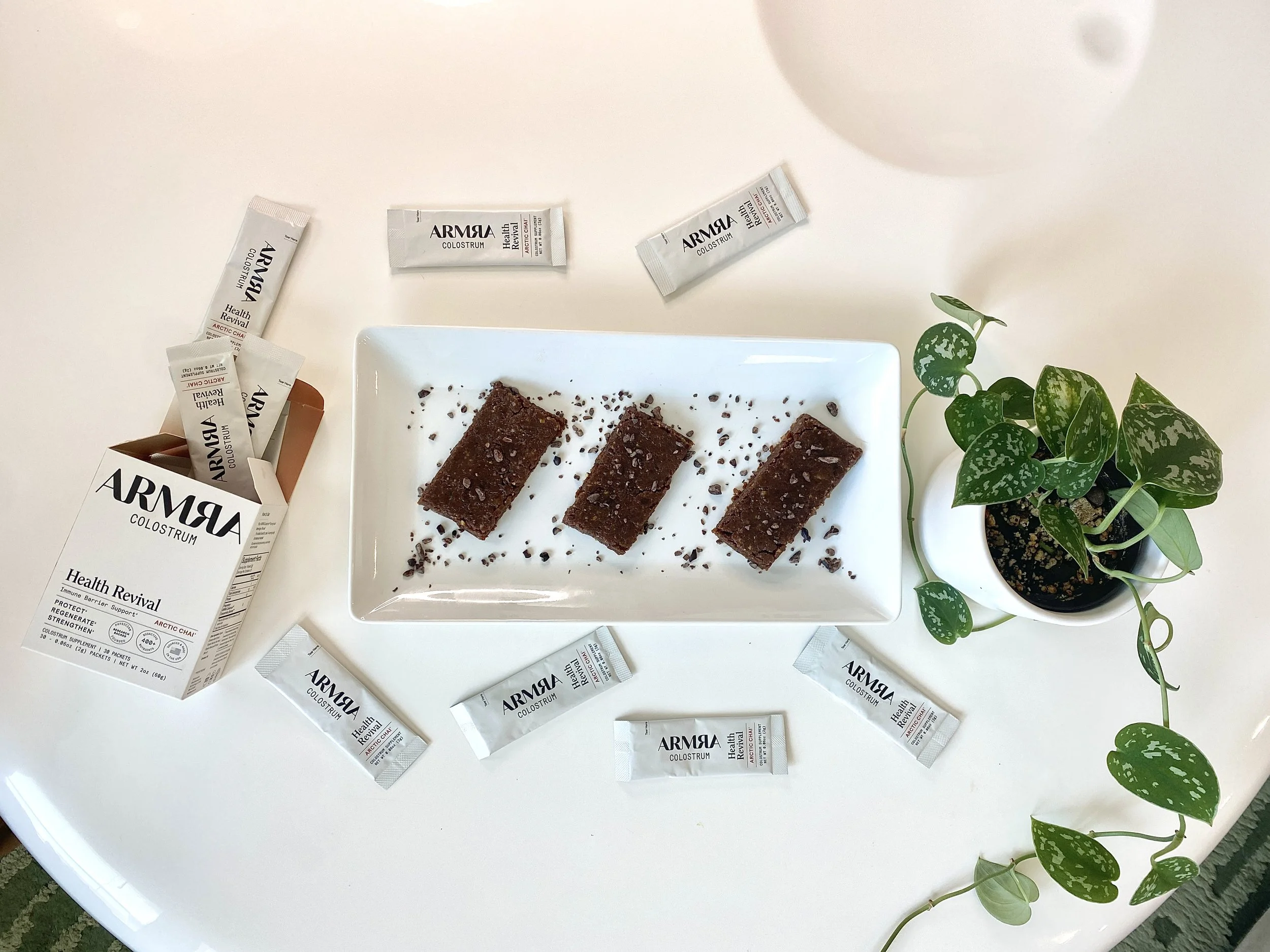 No bake date bars with Armra Colostrum packets styled on a white table with a plant