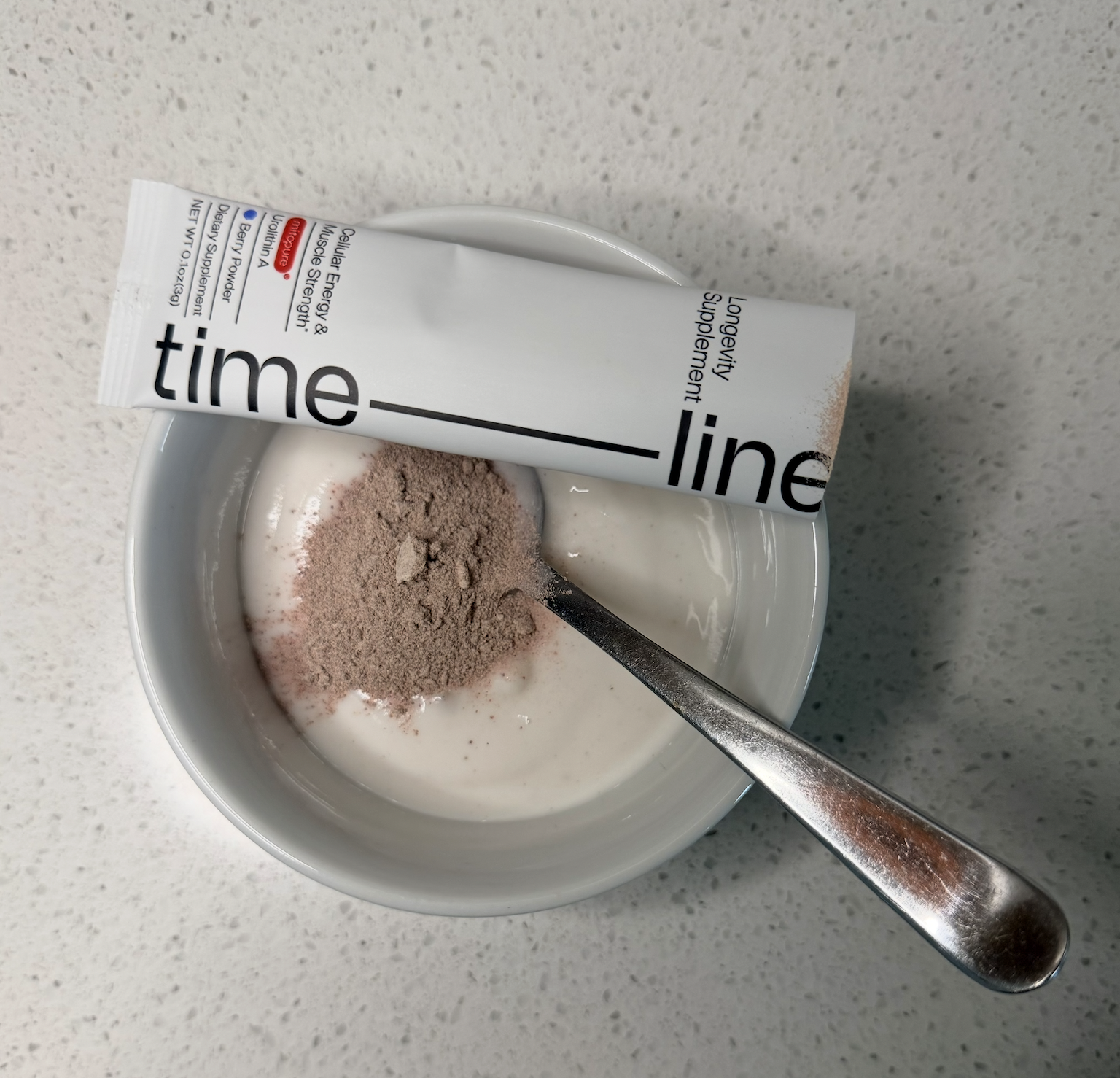 Timeline Mitopure berry powder mixed into a bowl of Harmless Harvest vanilla coconut yogurt with a spoon