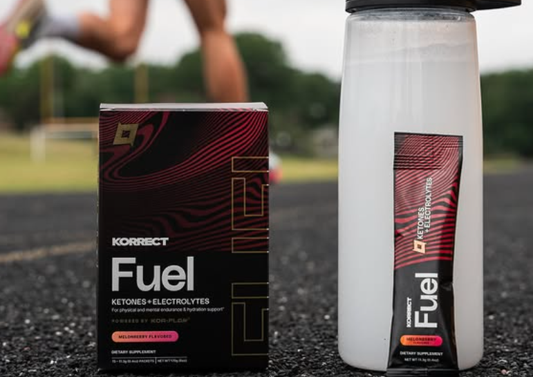 Korrect Fuel ketone and electrolyte supplement box and single-serve packet next to water bottle on running track before workout