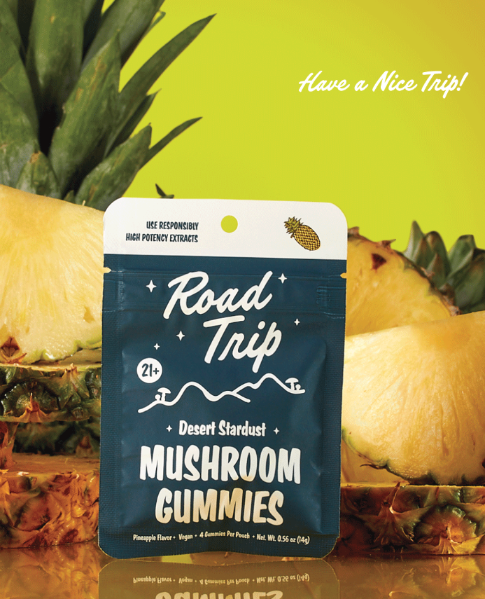Road Trip Desert Stardust Pineapple mushroom gummies pouch standing in front of sliced pineapple, with a Have a Nice Trip sign