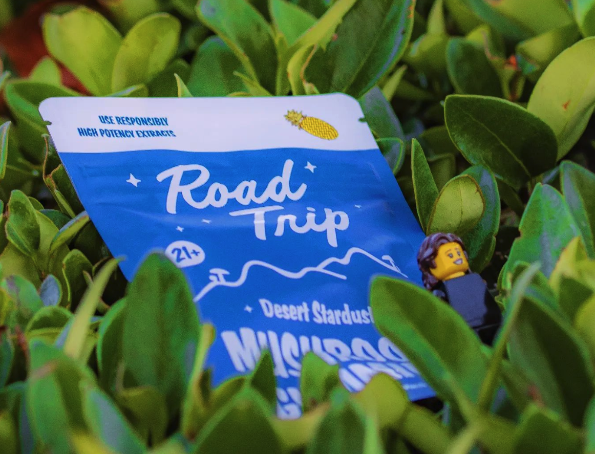 Road Trip Desert Stardust mushroom gummies pouch tucked into greenery, showing the 21+ high potency extract label