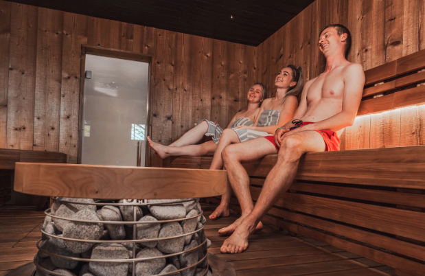 Friends sitting on wooden benches in a traditional steam sauna with hot rocks