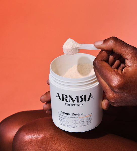 ARMRA colostrum powder scoop above container for gut health and immune support