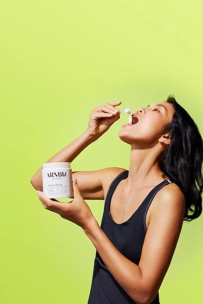 Woman taking a scoop of ARMRA Colostrum Immune Revival powder, highlighting daily immune and gut health support