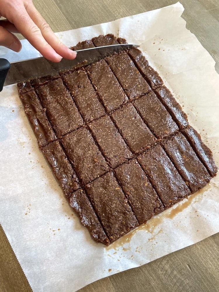 Slicing chilled no bake date bars into even squares on parchment paper