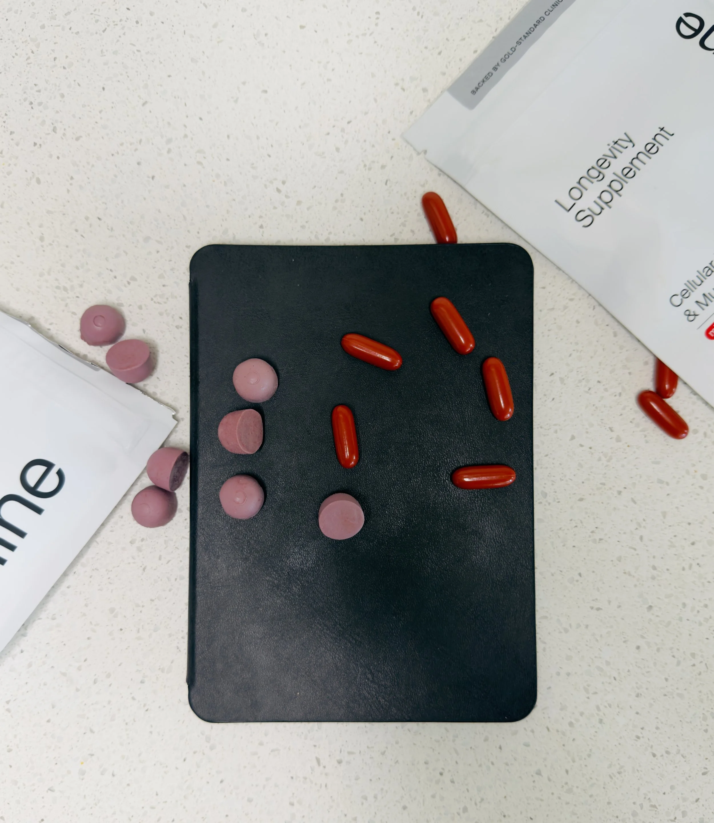Timeline Mitopure gummies and softgel capsules scattered on a dark surface next to the Longevity Supplement pouches