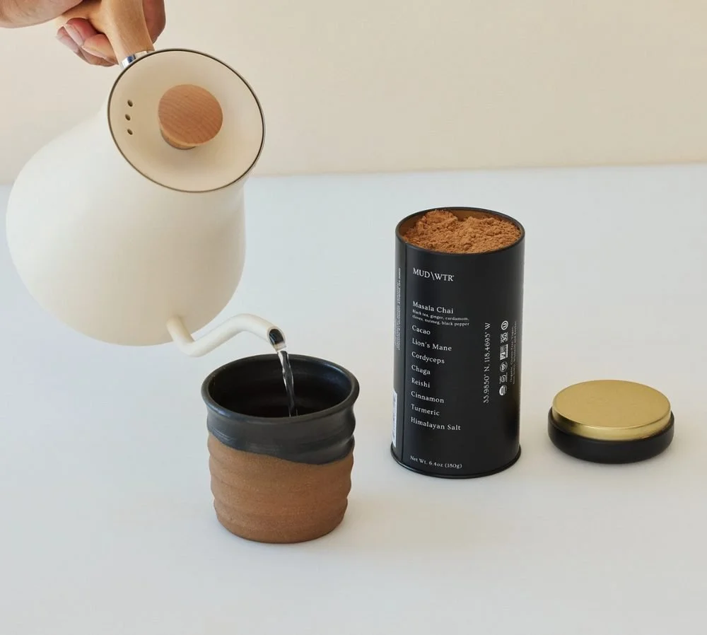 MUD WTR being poured from a kettle into a cup beside the tin