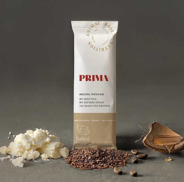 Prima Salted Caramel protein bar standing next to its raw whole food ingredients, grass fed tallow, cacao nibs, coconut, and honey