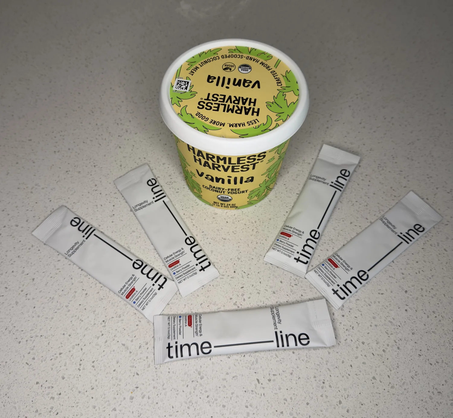 A tub of Harmless Harvest vanilla coconut yogurt with five Mitopure powder sachets fanned out around it