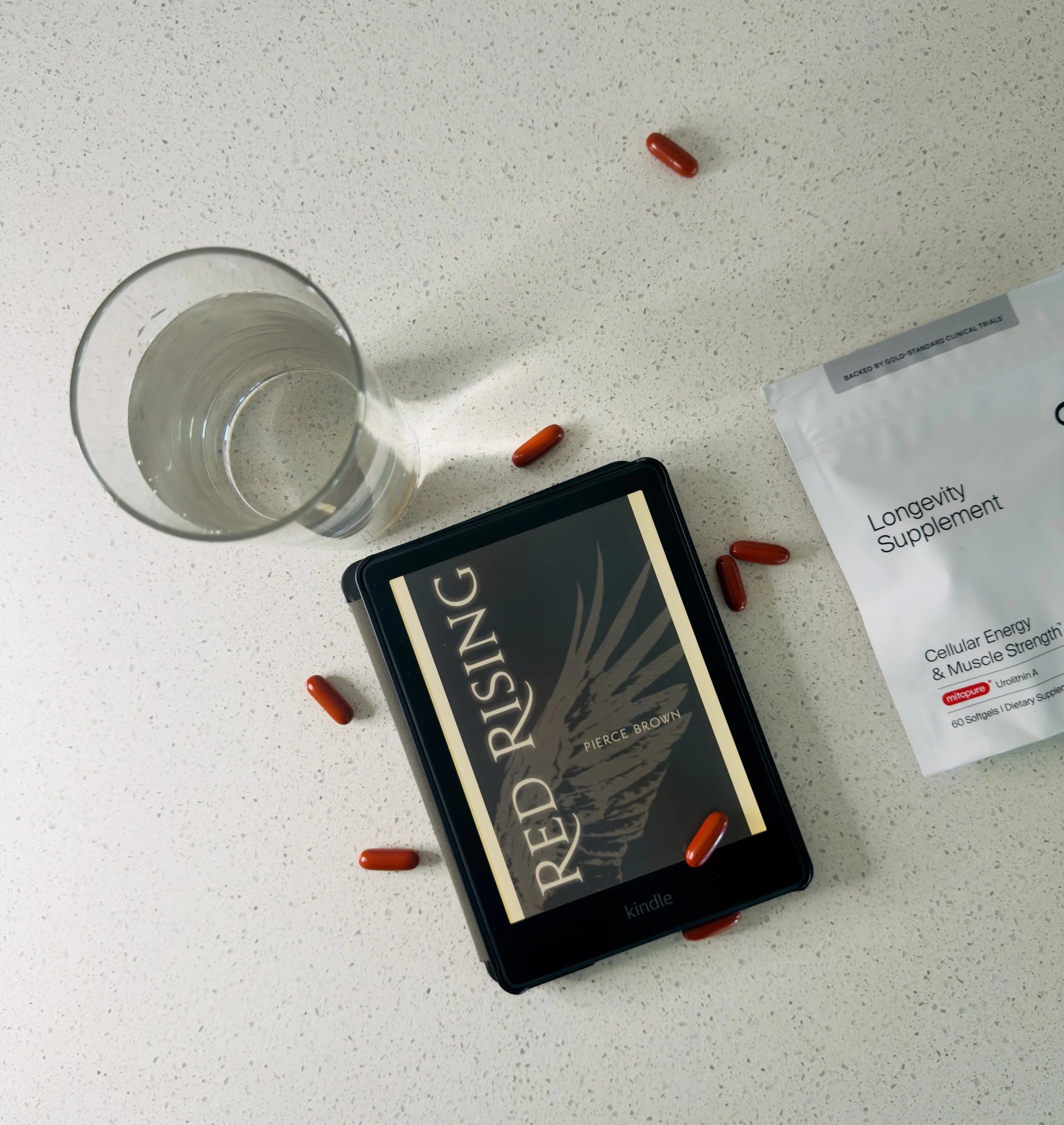Timeline Mitopure softgel capsules next to a Kindle e-reader and a glass of water
