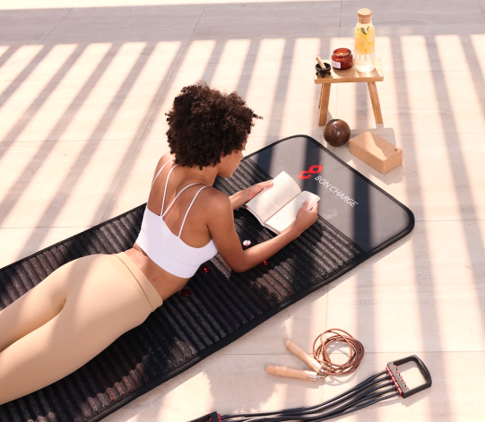 Woman relaxing and reading a book while lying on the Bon Charge PEMF Mat outdoors