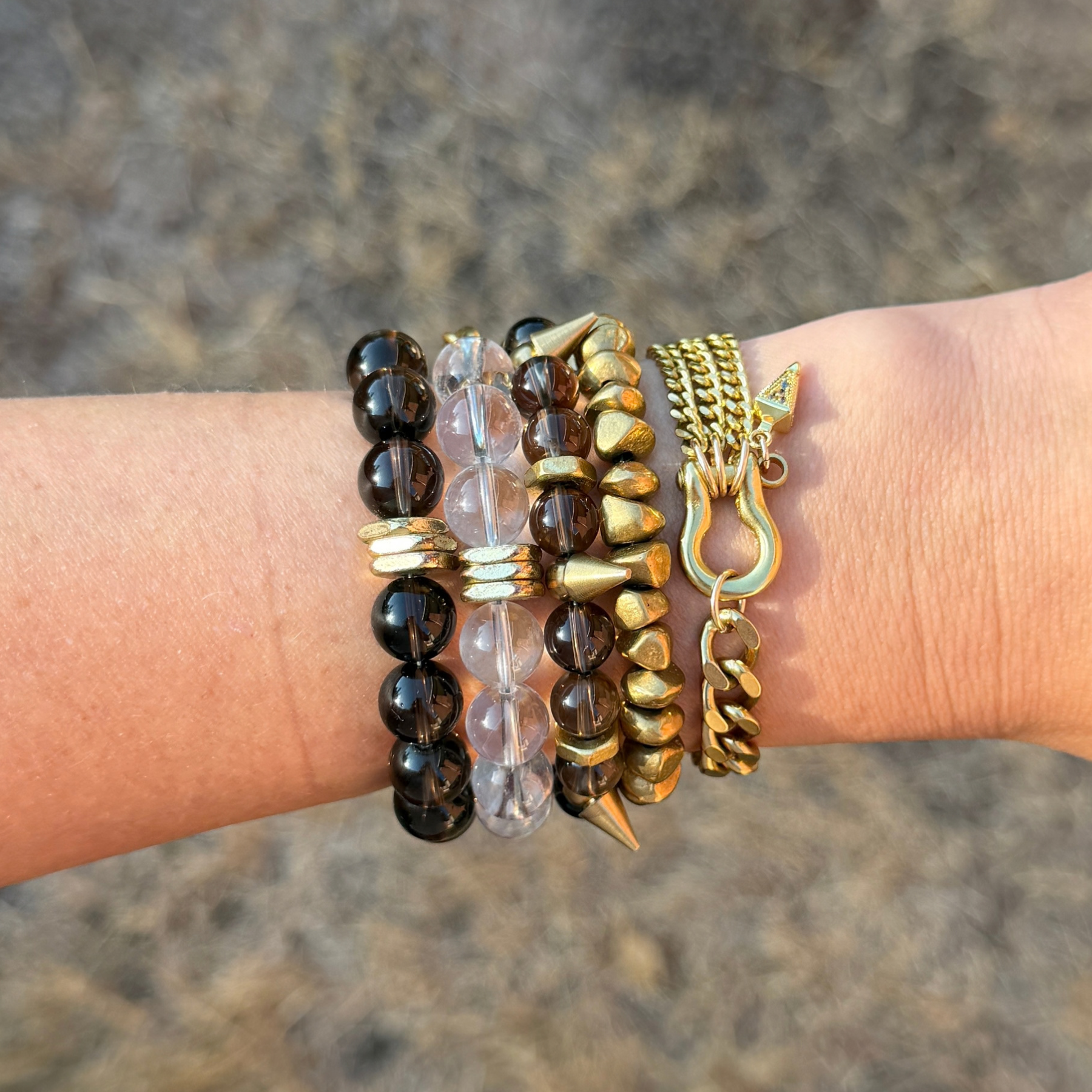 Close-up of a person's wrist wearing multiple gold and beaded bracelets, with a blurry background.