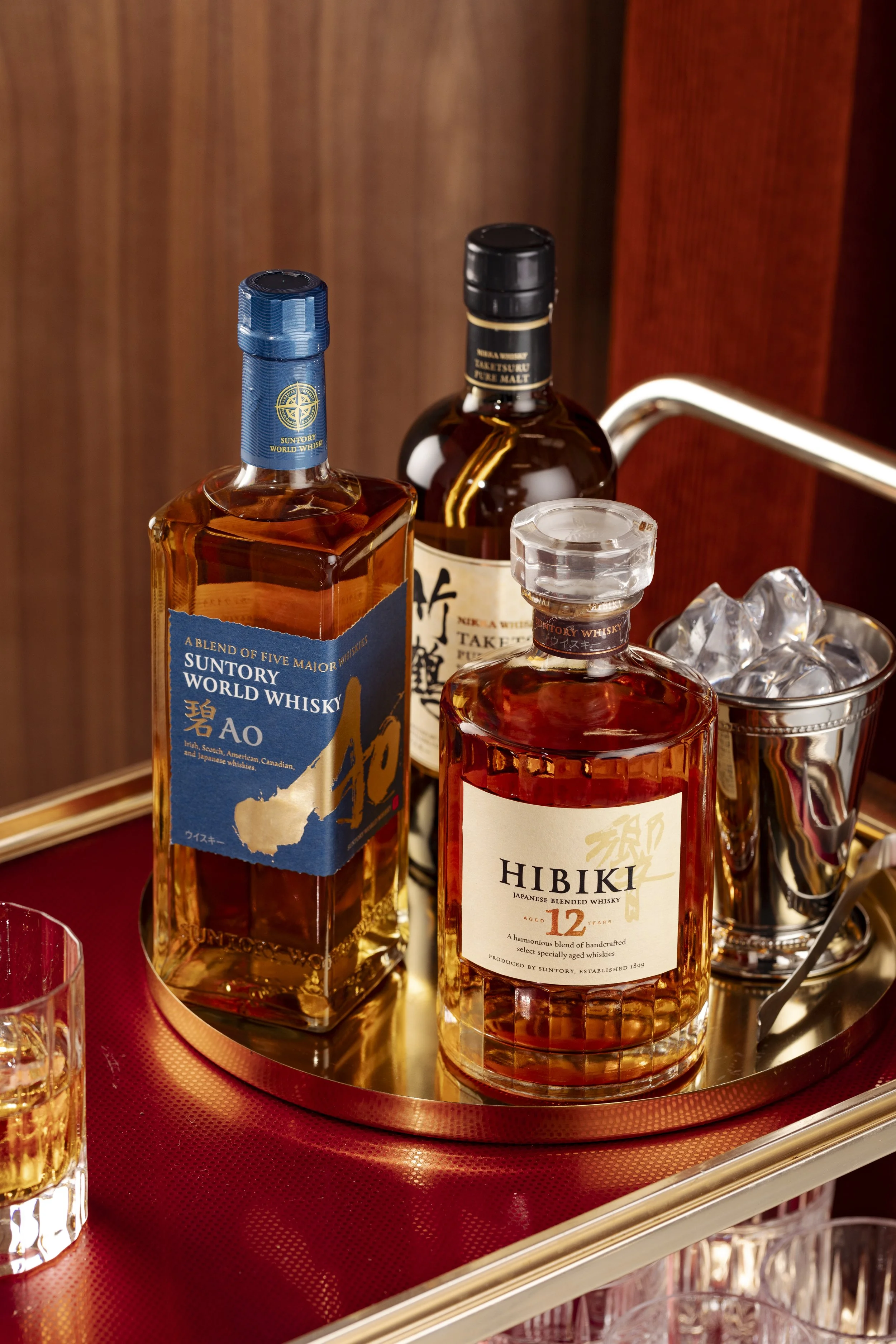 Two bottles of Japanese whisky and one bottle of Irish whisky on a tray with ice and glasses in the background.