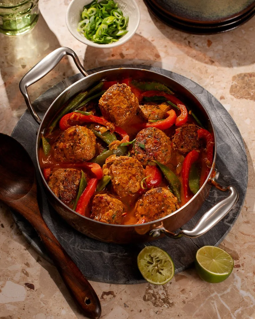 Meatballs with red and green bell peppers in a tomato sauce, garnished with lime halves.