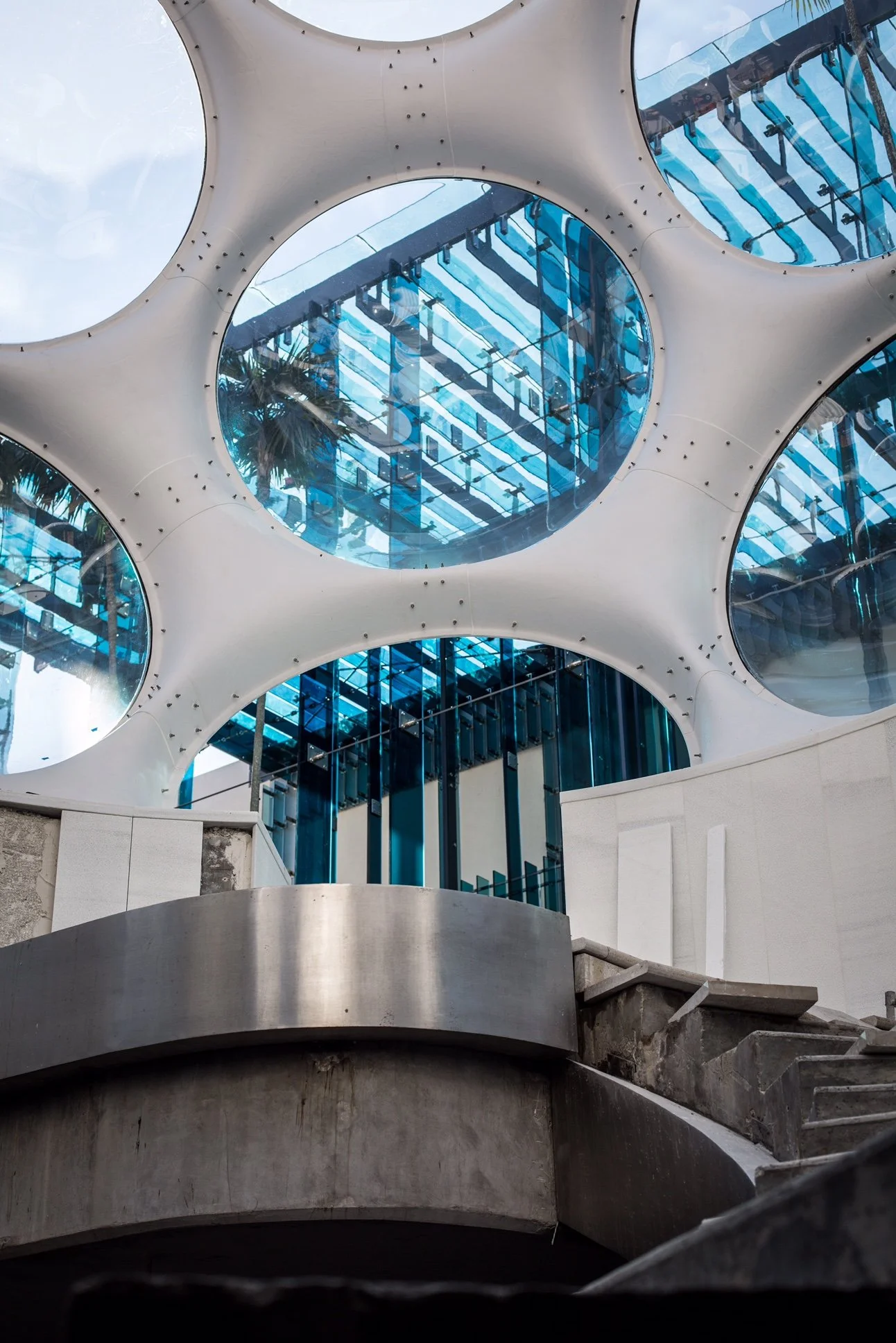   “The Fly’s Eye Dome creates a striking gateway to the underground parking garage, its sculptural form amplified by Sou Fujimoto’s shimmering blue glass façade. Together, they transform Palm Court into a spatial experience that’s both futuristic and