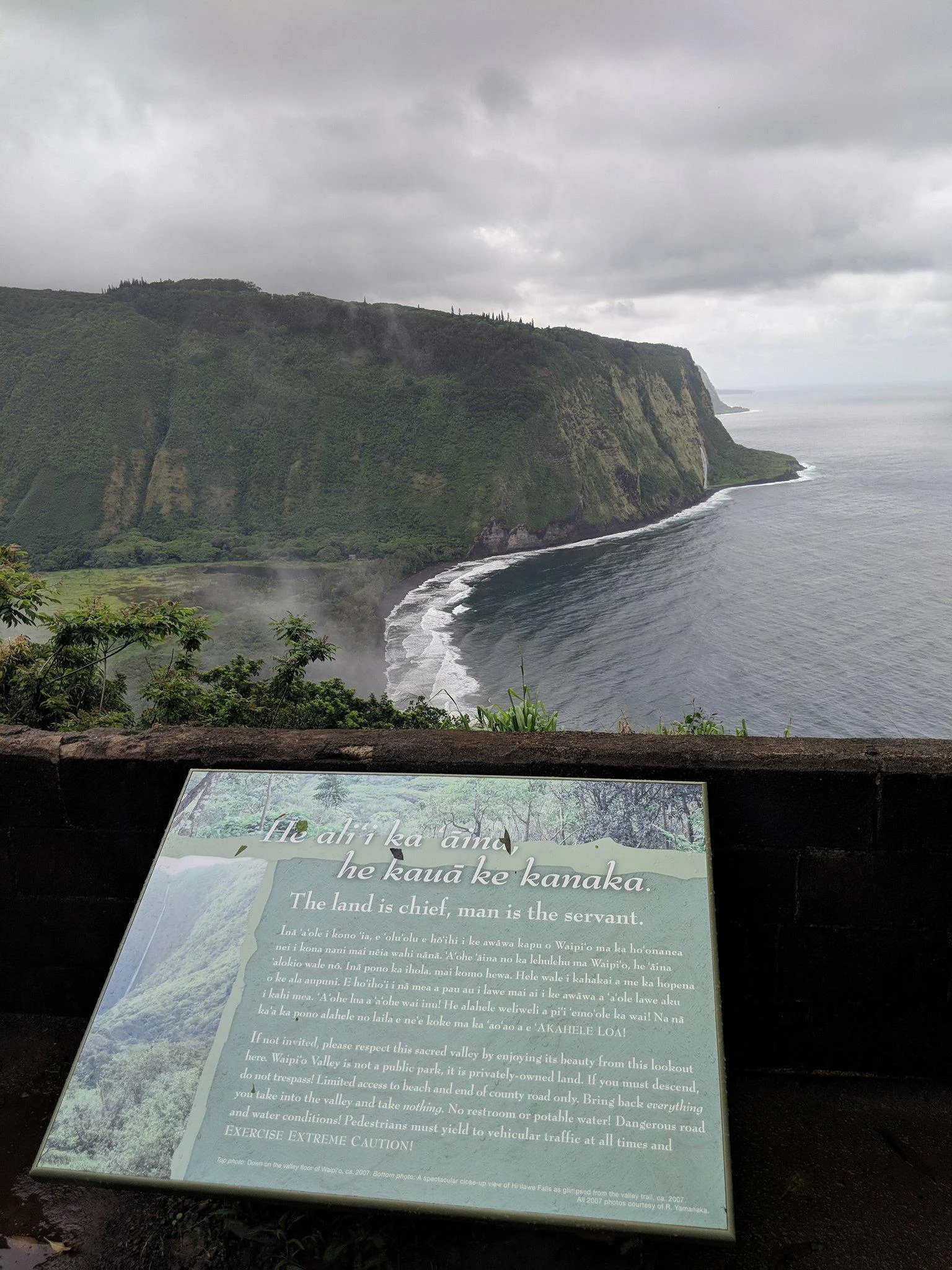 Image Description: Waipi'o Valley with Placard reading, in part: "If not invited, please respect this sacred valley by enjoying its beauty from this lookout here. Waipi'o Valley is not a public park, it is privately-owned land. If you must descend, do not trespass!"