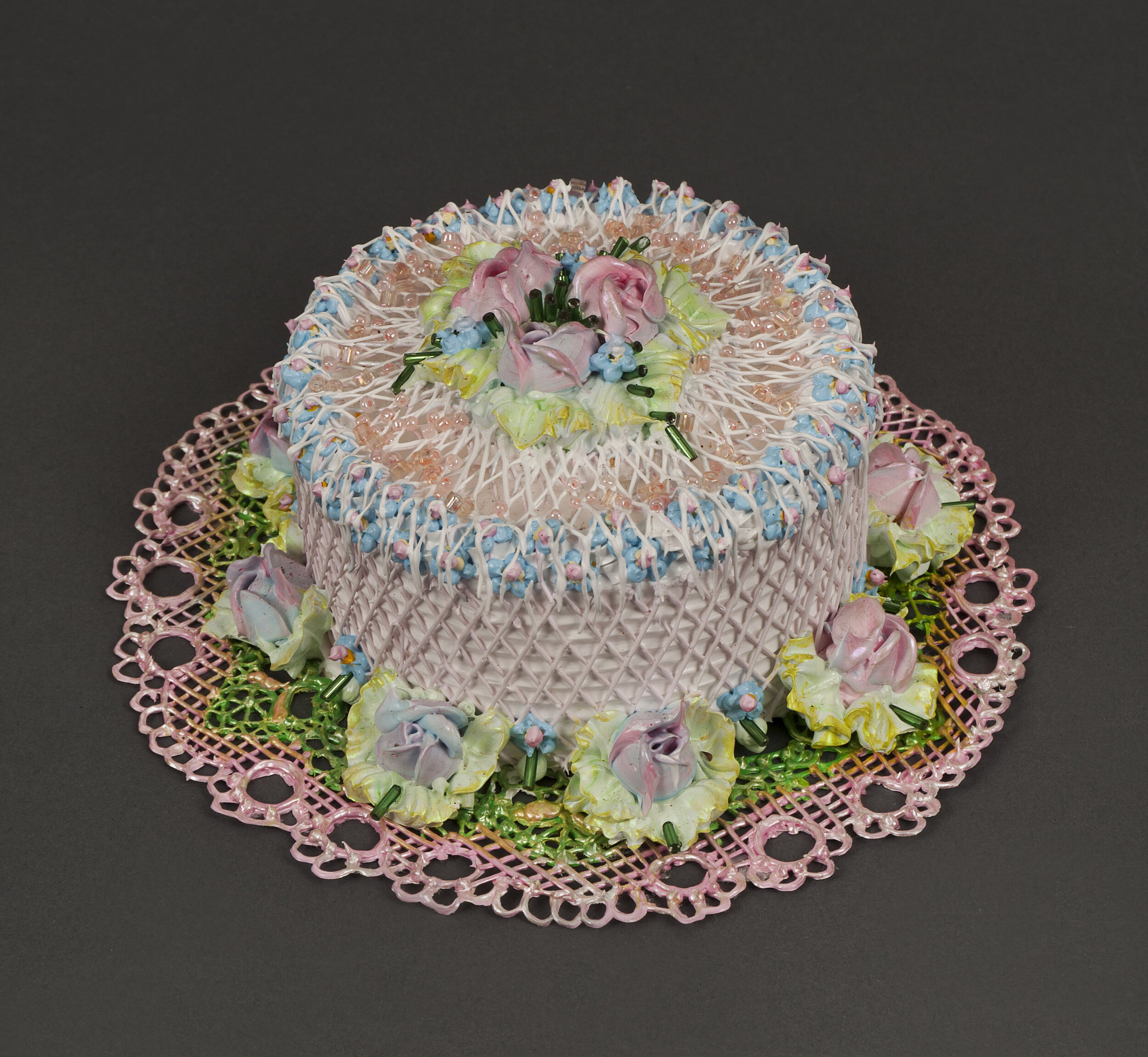 Multi-colored cake decorated with roses, strings of pink icing, and beads on a pink doily