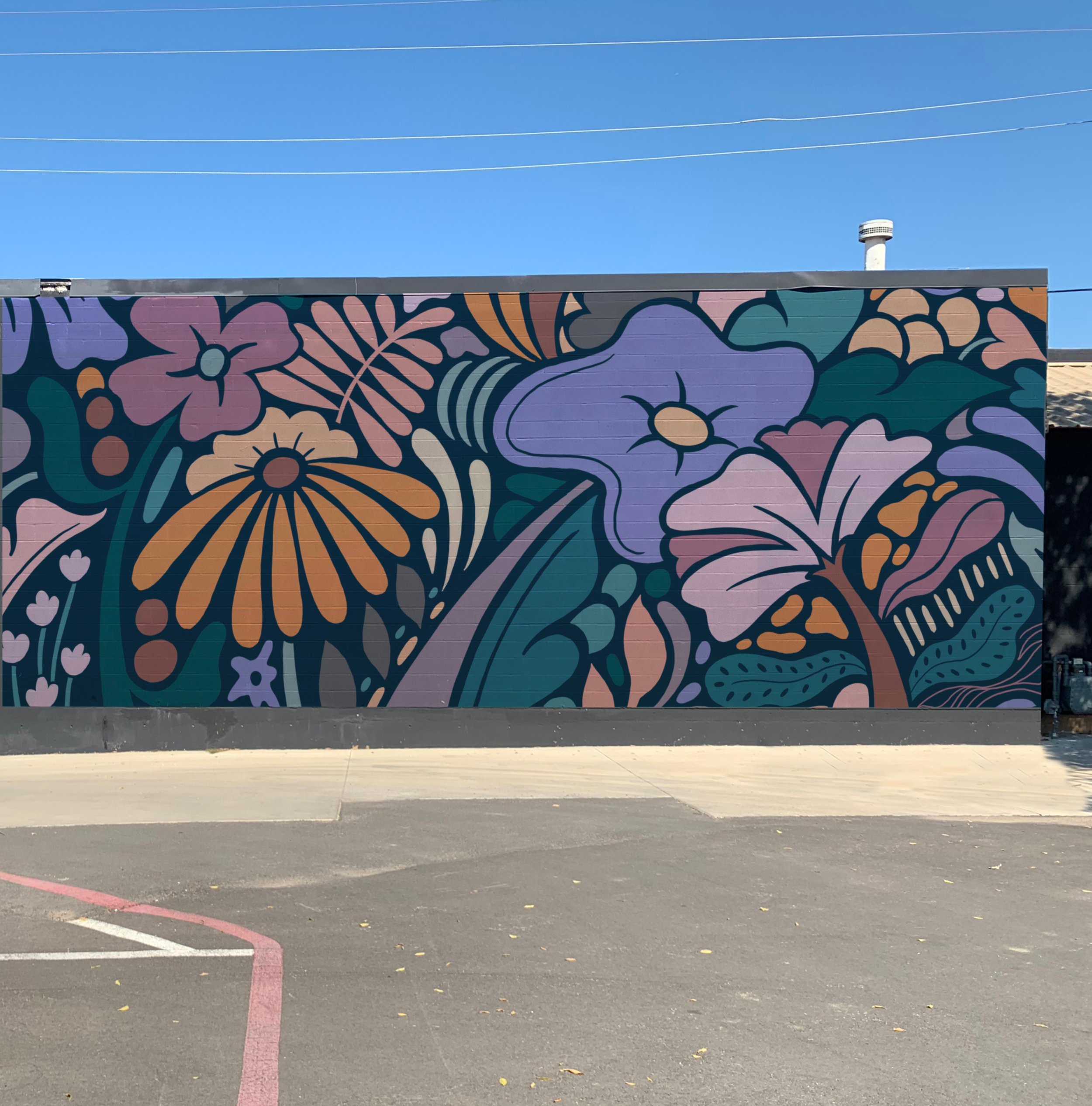 Colorful mural of abstract floral design on a brick wall under a clear blue sky.