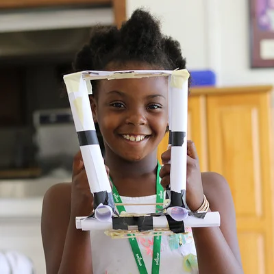 A child holds up a model bridge she built in STEM camp.