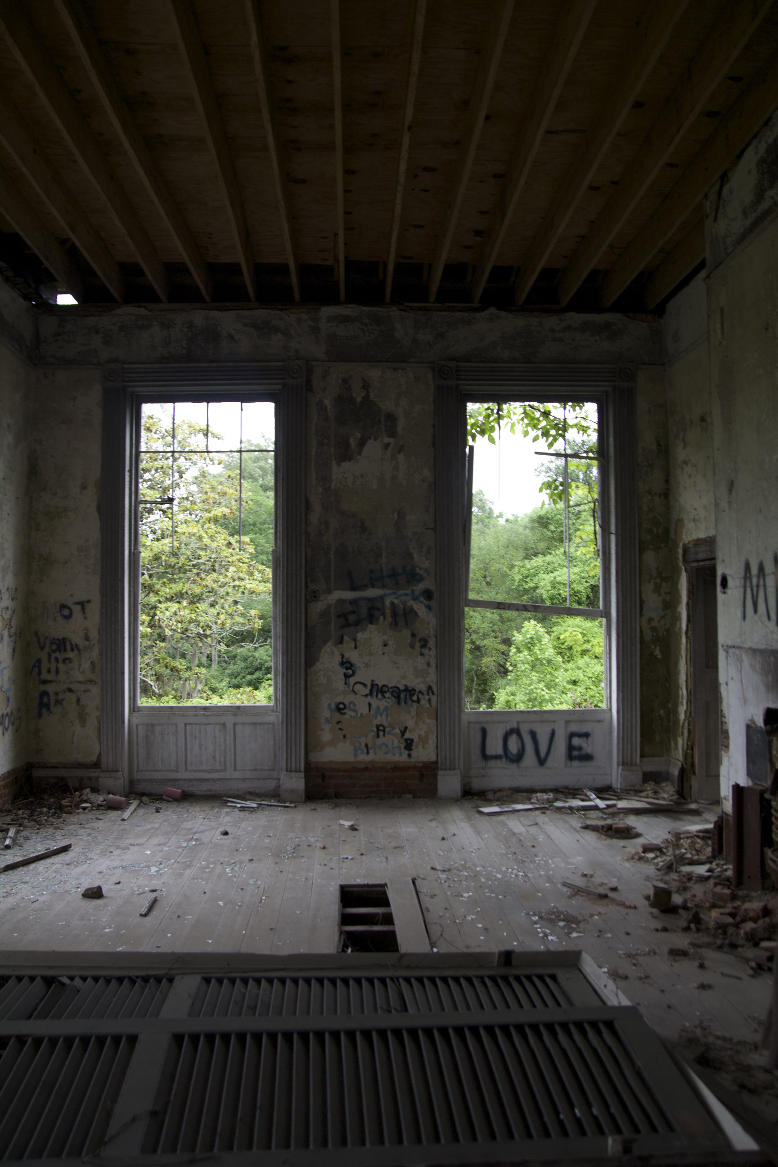 2nd floor bedroom with windows missing and graffiti. The exposed beams you see above are from the new roof that was put on after the 2002 fire. The shutters you see on the ground used to adorn the front windows.
