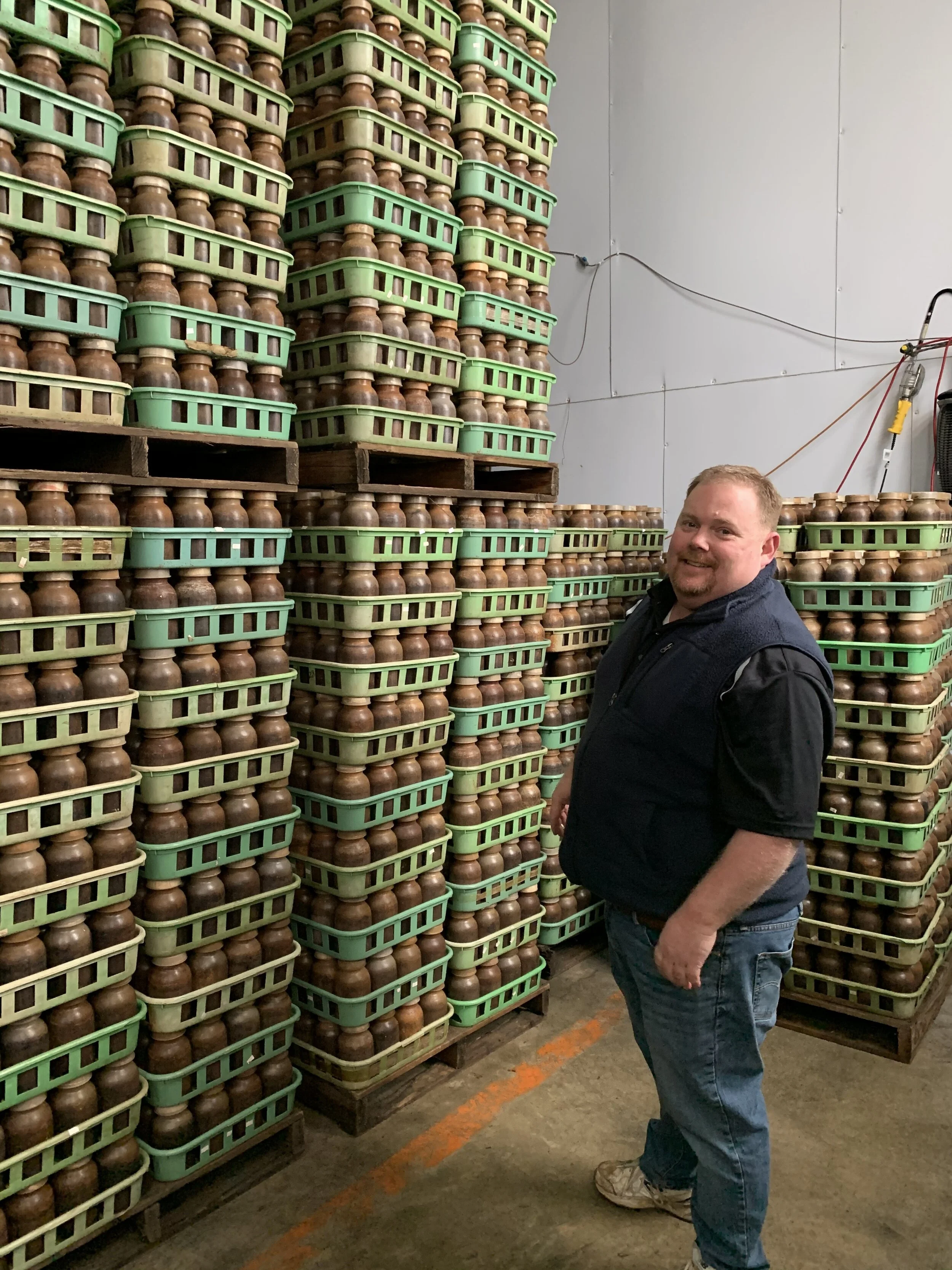 Owner Chris Becker is pictured here alongside just a portion of one weeks worth of mushrooms, these still in the spawning stage (thus, the jars still have their lids on). This room was warm, like standing on the beach in Mexico ;). Image Courtesy: Dan Meyers
