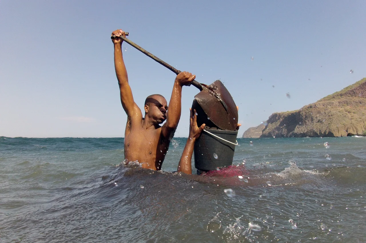 Ja gets her bucket filled with sand. The bucket weights about 20 kilos. Wind and currents are often very strong and the temperature of the sea is around 20 degrees. Charco, Ribeira da Barca, Santiago, Cape Verde