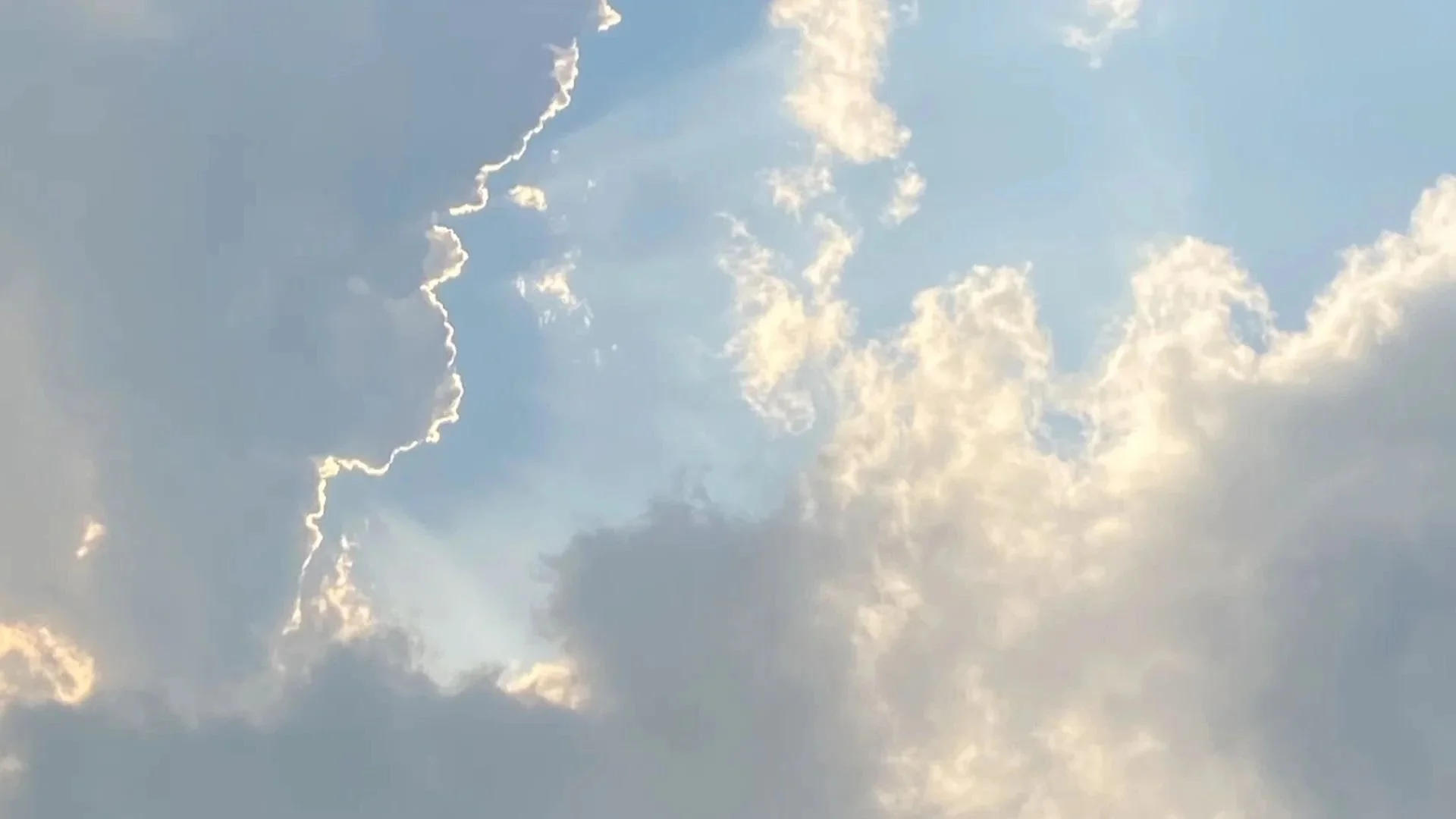 Soft blue sky with sun rays breaking through layered clouds