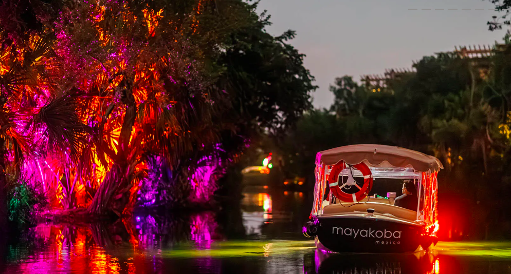 Embarcación en un canal de Mayakoba junto a vegetación iluminada, en una imagen difundida para su programa de Día de Muertos.