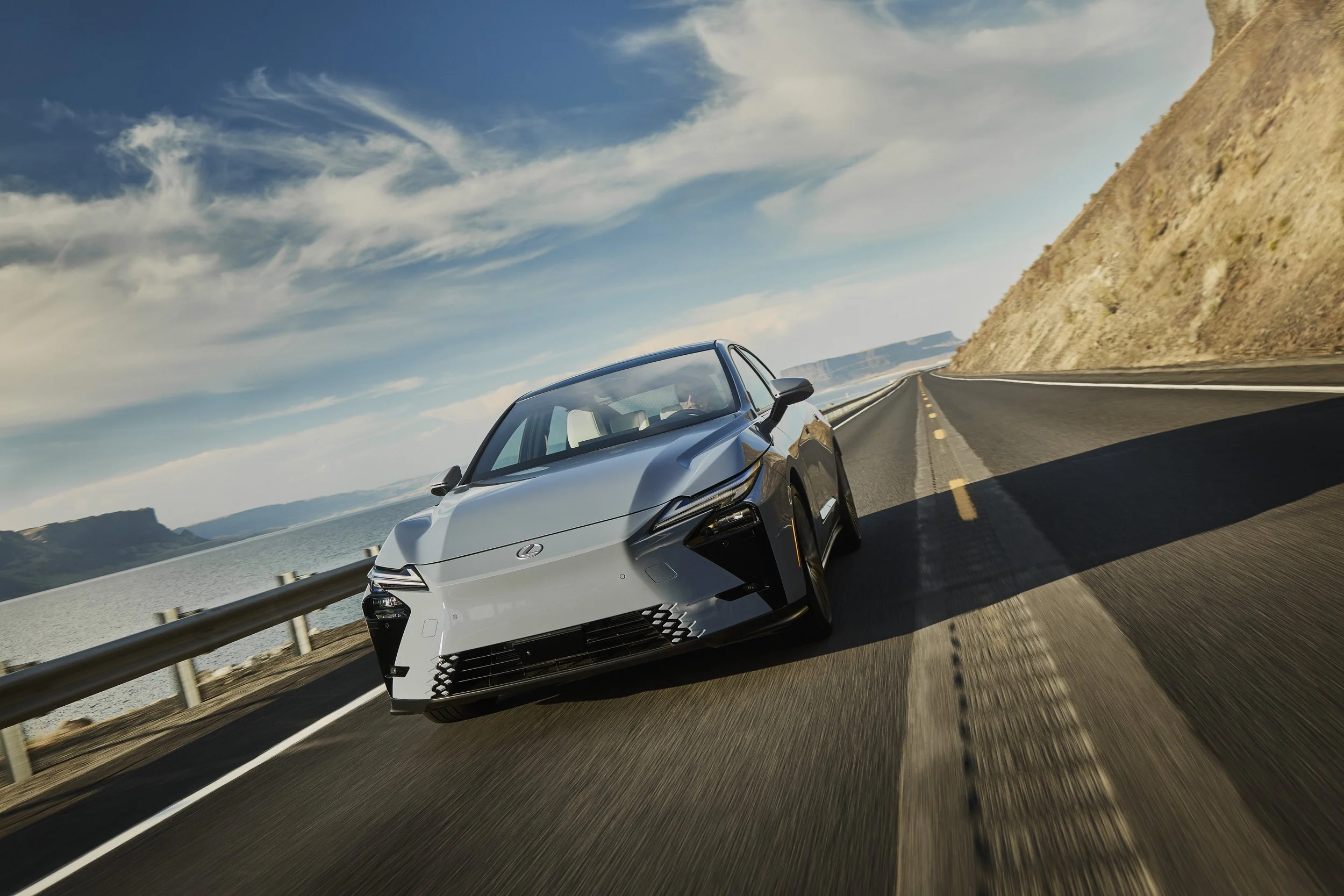 Lexus ES 350h plateado circulando por una carretera junto al mar