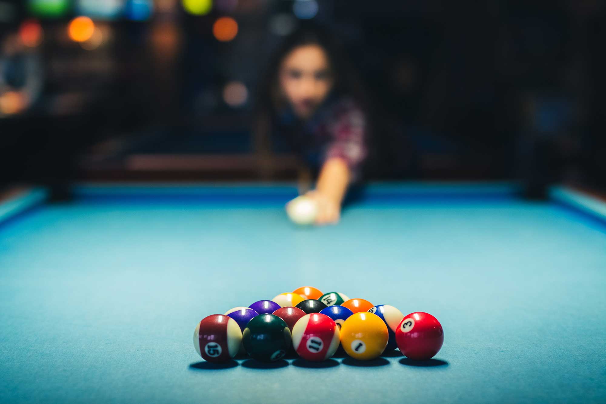 Woman at a pool table, taking aim at the balls.