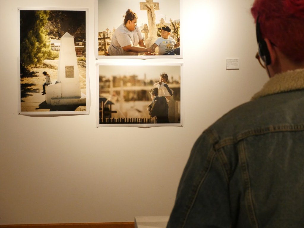 Viewers watch a video about Día de los Muertos in Juarez in front of photographs of families visiting cemeteries. Image courtesy of the artists.