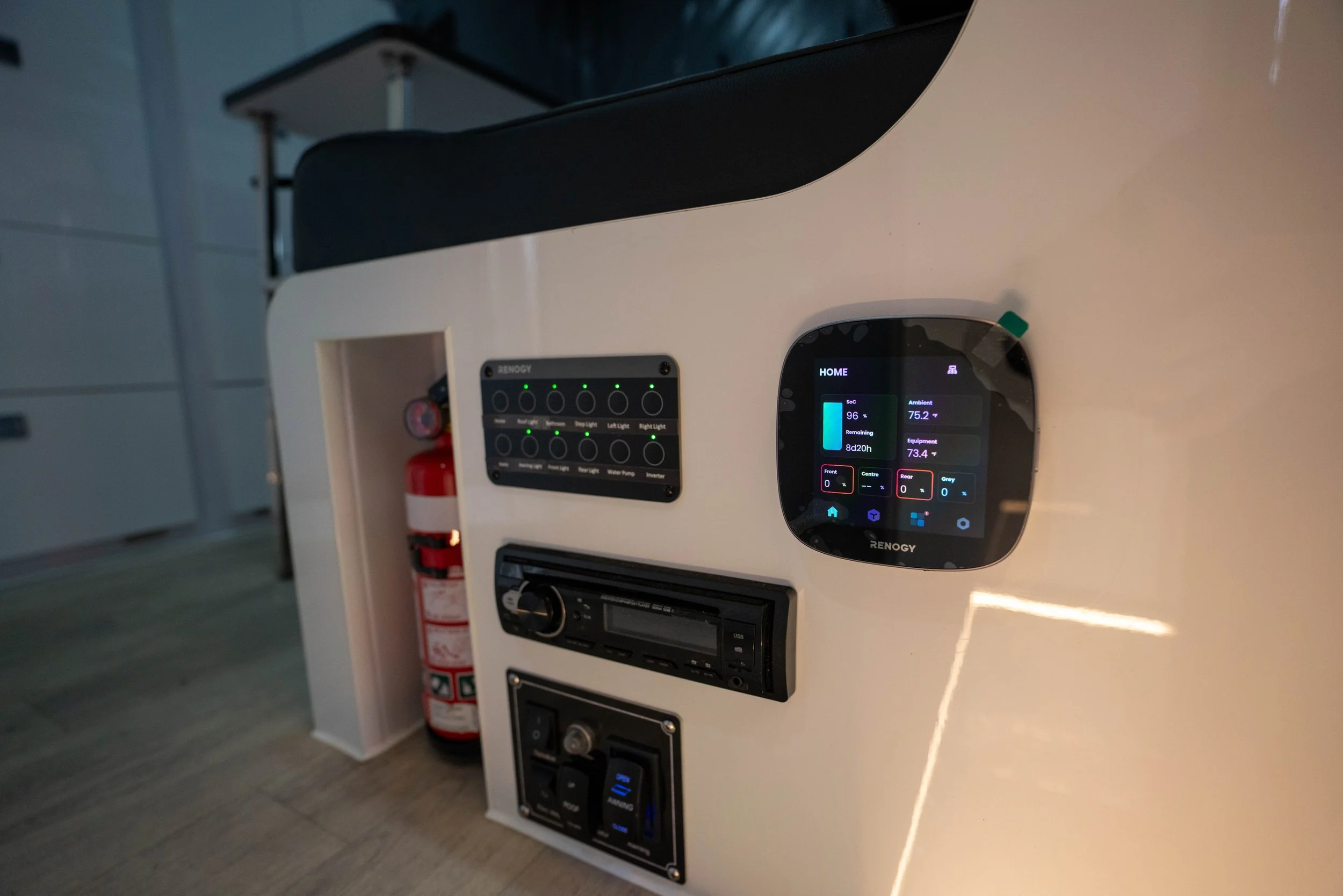 Close-up of a control panel with digital display, switches, and knobs mounted on a white surface, with fire extinguisher bottle partially visible in the background.