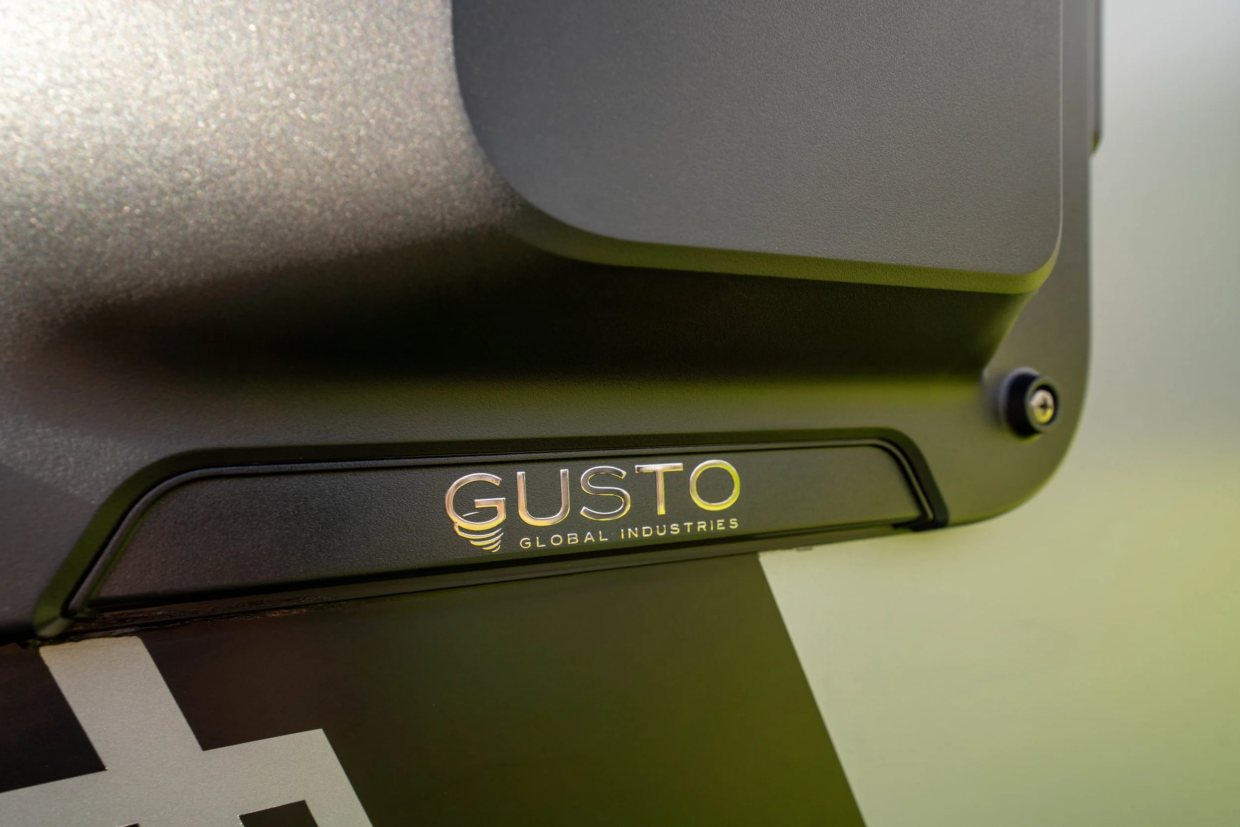 Close-up of a black electronic device with a label that reads 'GUSTO Global Industries,' positioned over a black and white striped surface.