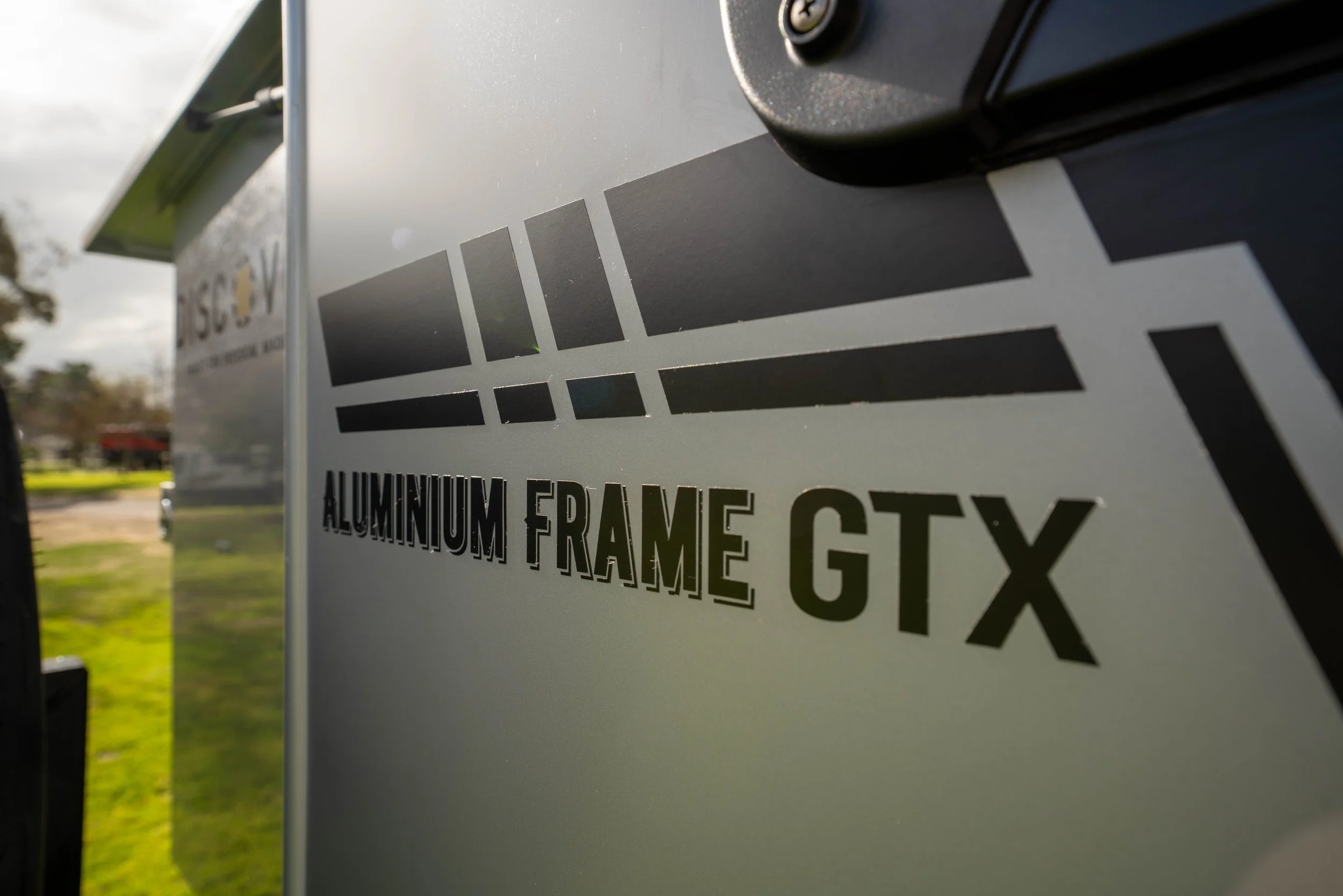 Close-up of a sign indicating aluminum frame gateway, with part of a vehicle visible in the background.