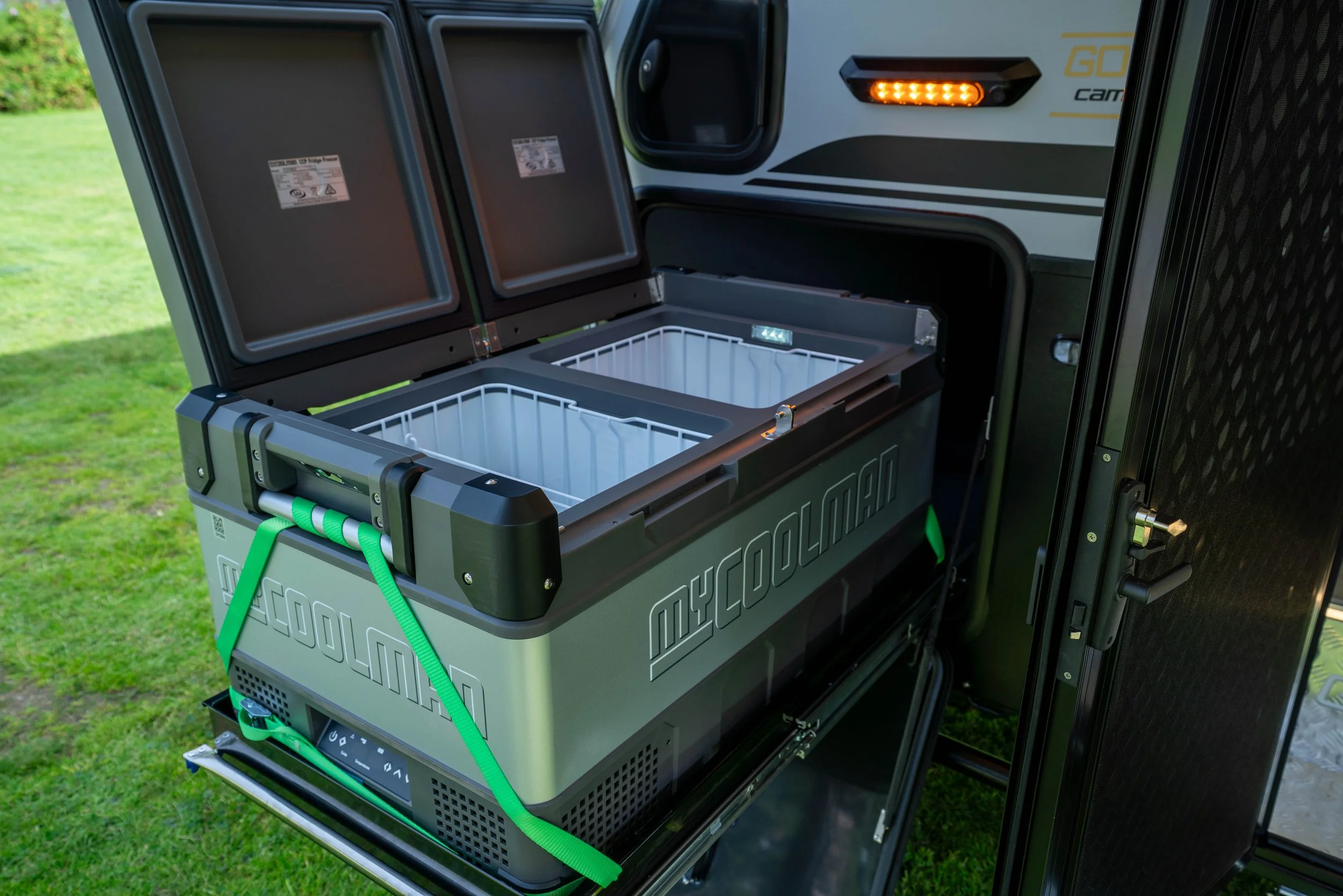 Open portable refrigeration unit mounted on a vehicle, with empty interior compartments and a control panel at the front, outdoors on grass.