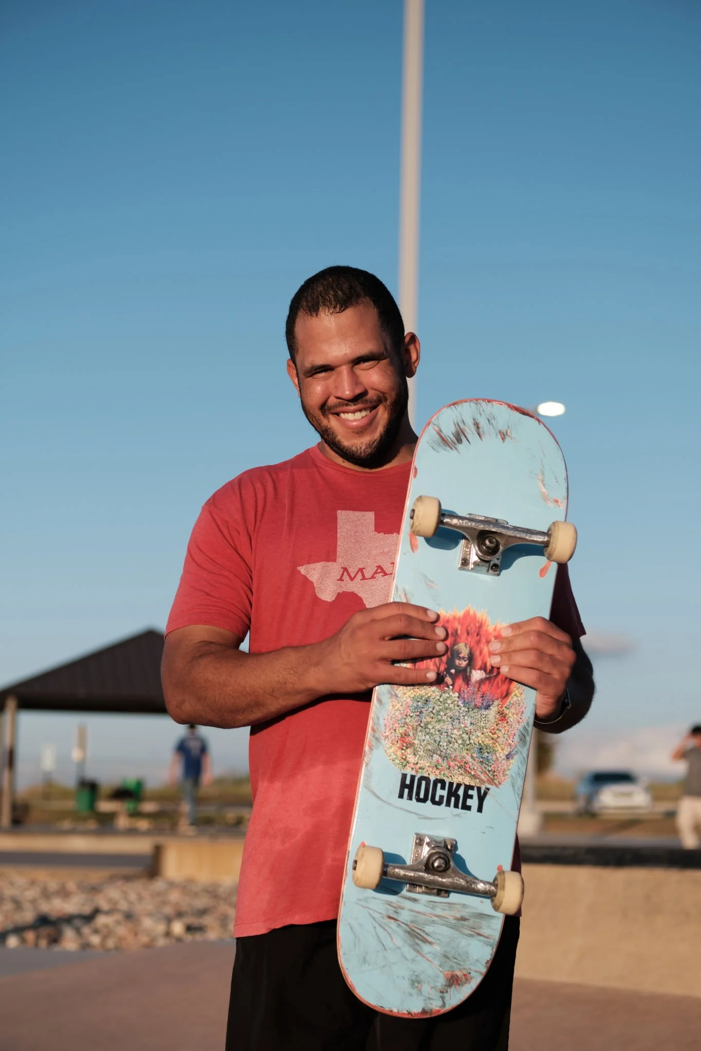 Jared Stevenson at the skatepark, holding his skateboard and smiling