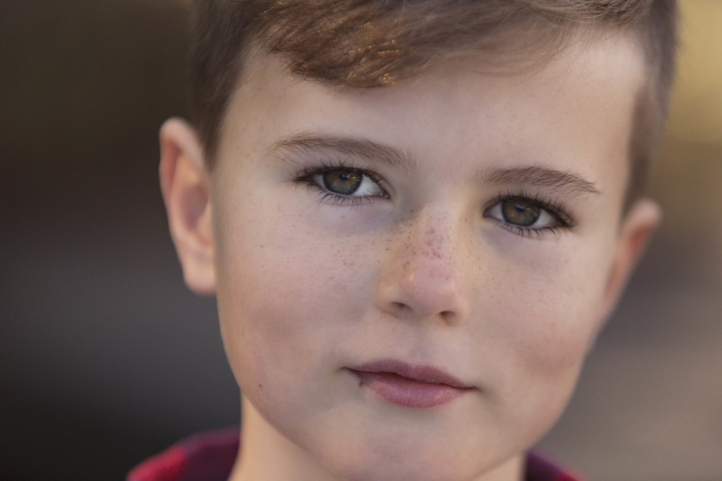A photo of a young boy with a beautiful brown eyes, freckles and a smidge of a smile