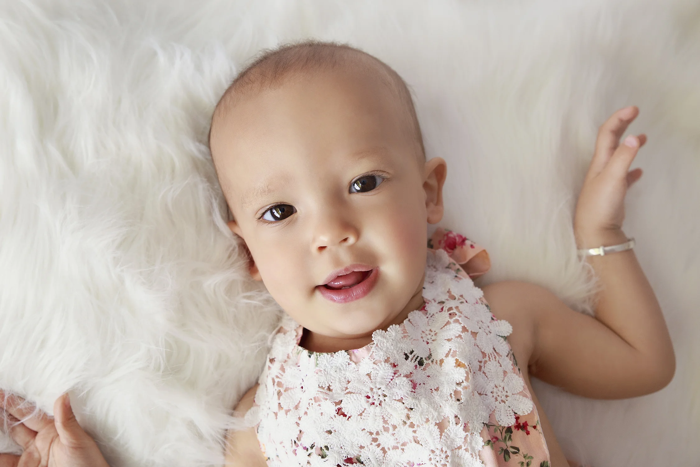 A sweet baby girl smiling on a white fluffy rug