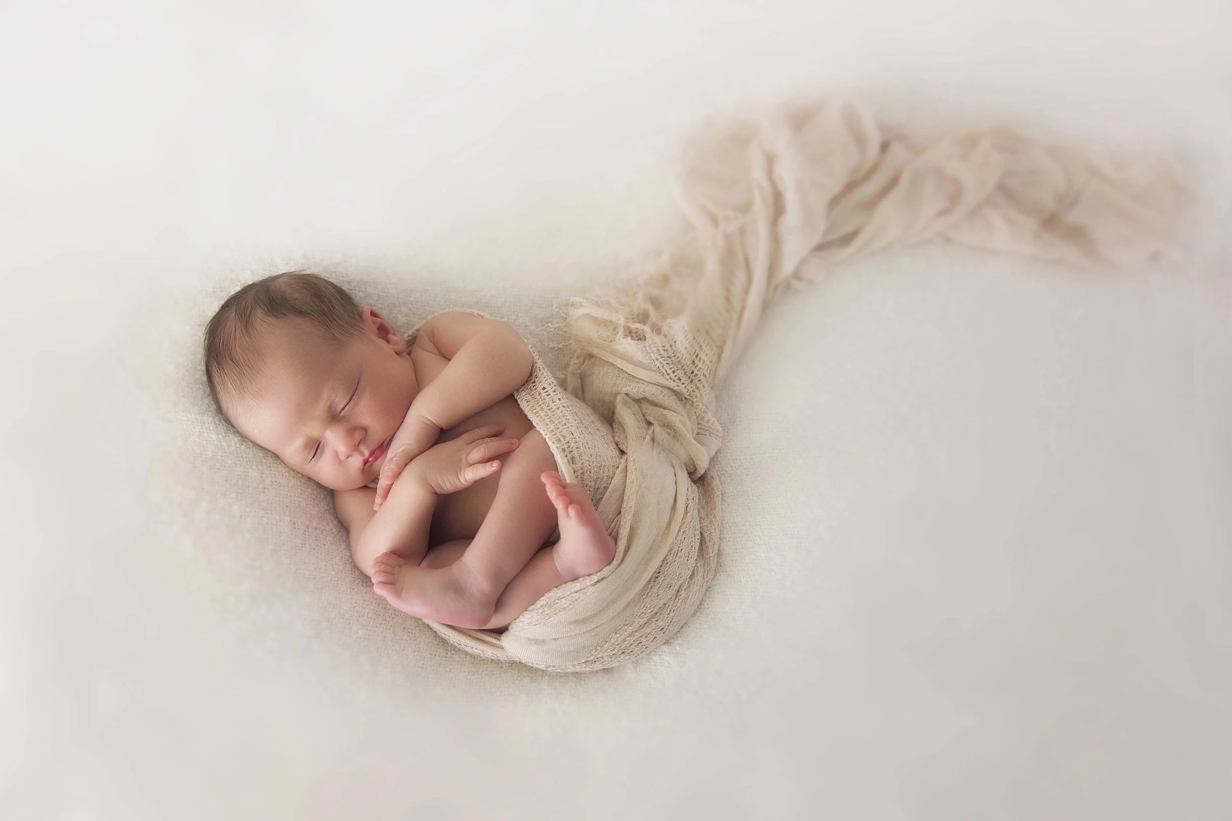 A baby girl wrapped in a soft peach wrap on a cream blanket