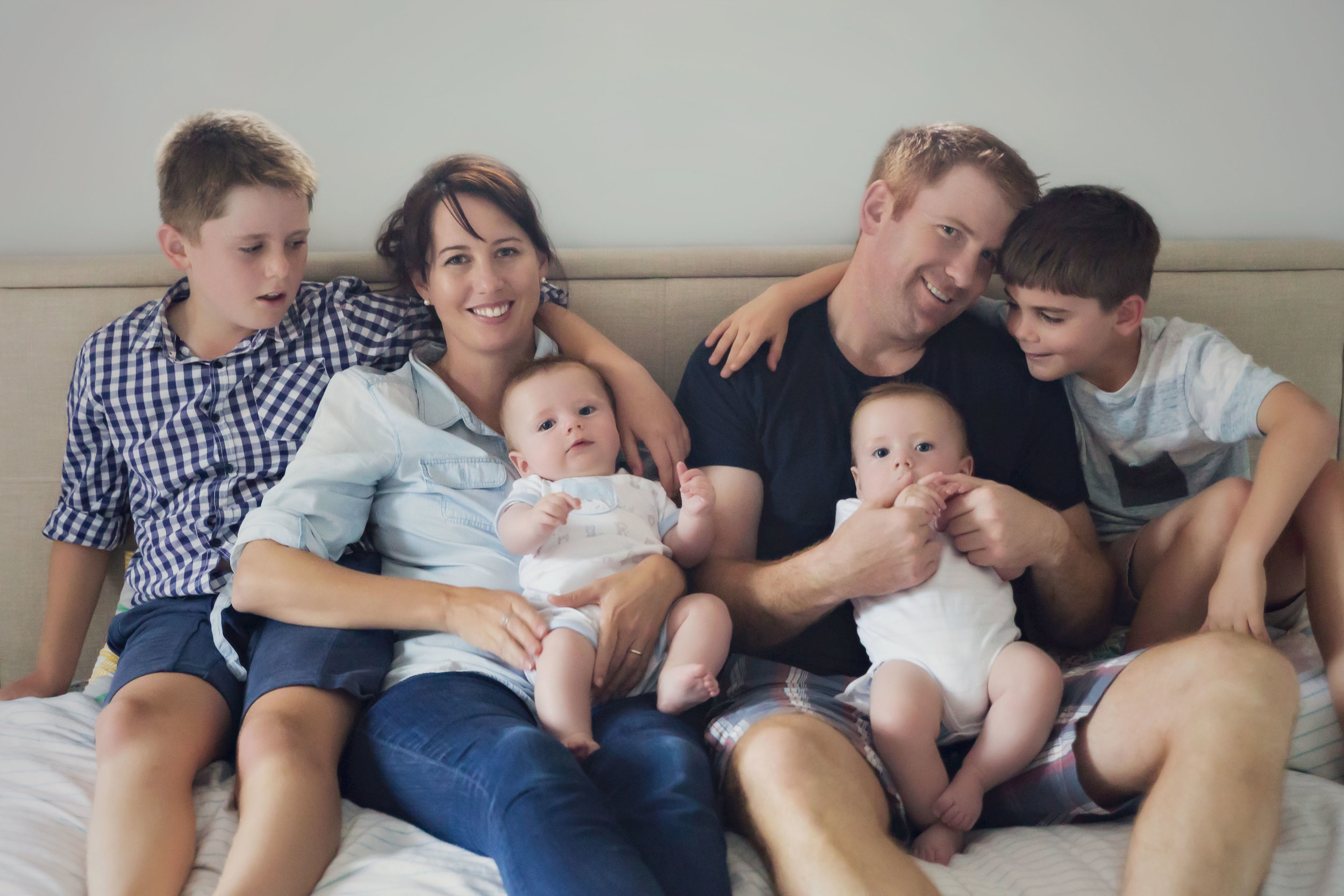 A family lifestyle portrait of Mum and Dad and their four boys cuddling and smiling on their bed