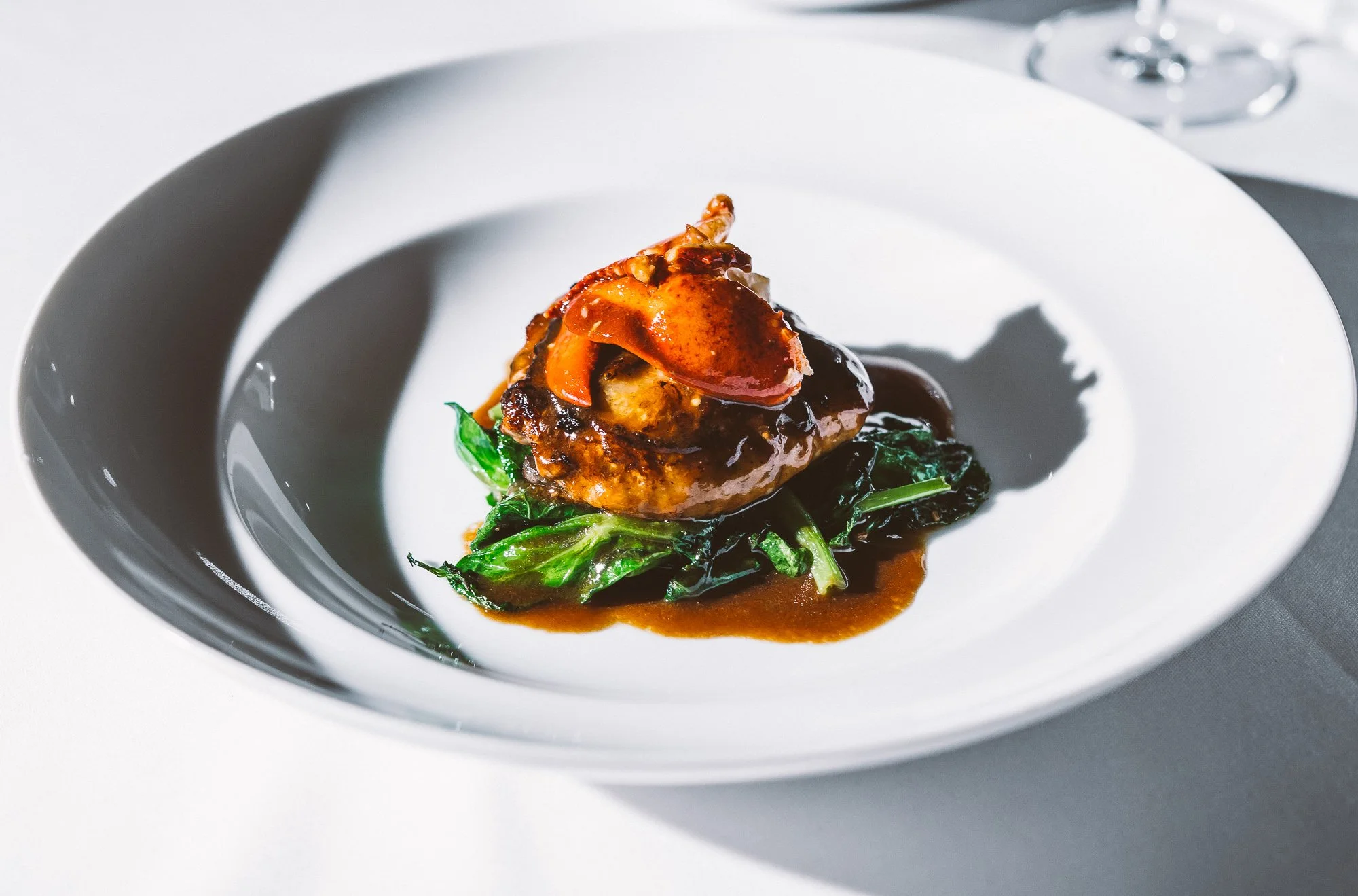 A plated gourmet dish featuring a piece of meat topped with sauce and garnished with vegetables, served on a white plate.