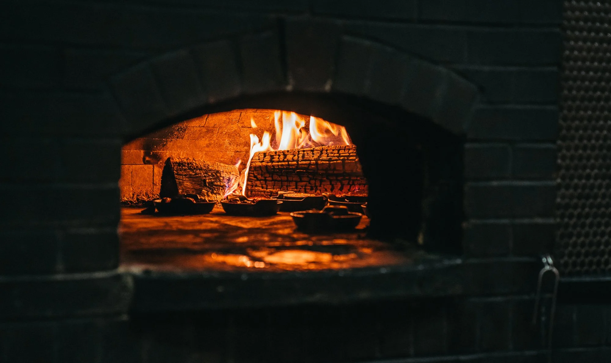 A brick fireplace with burning logs and visible flames, cooking inside.