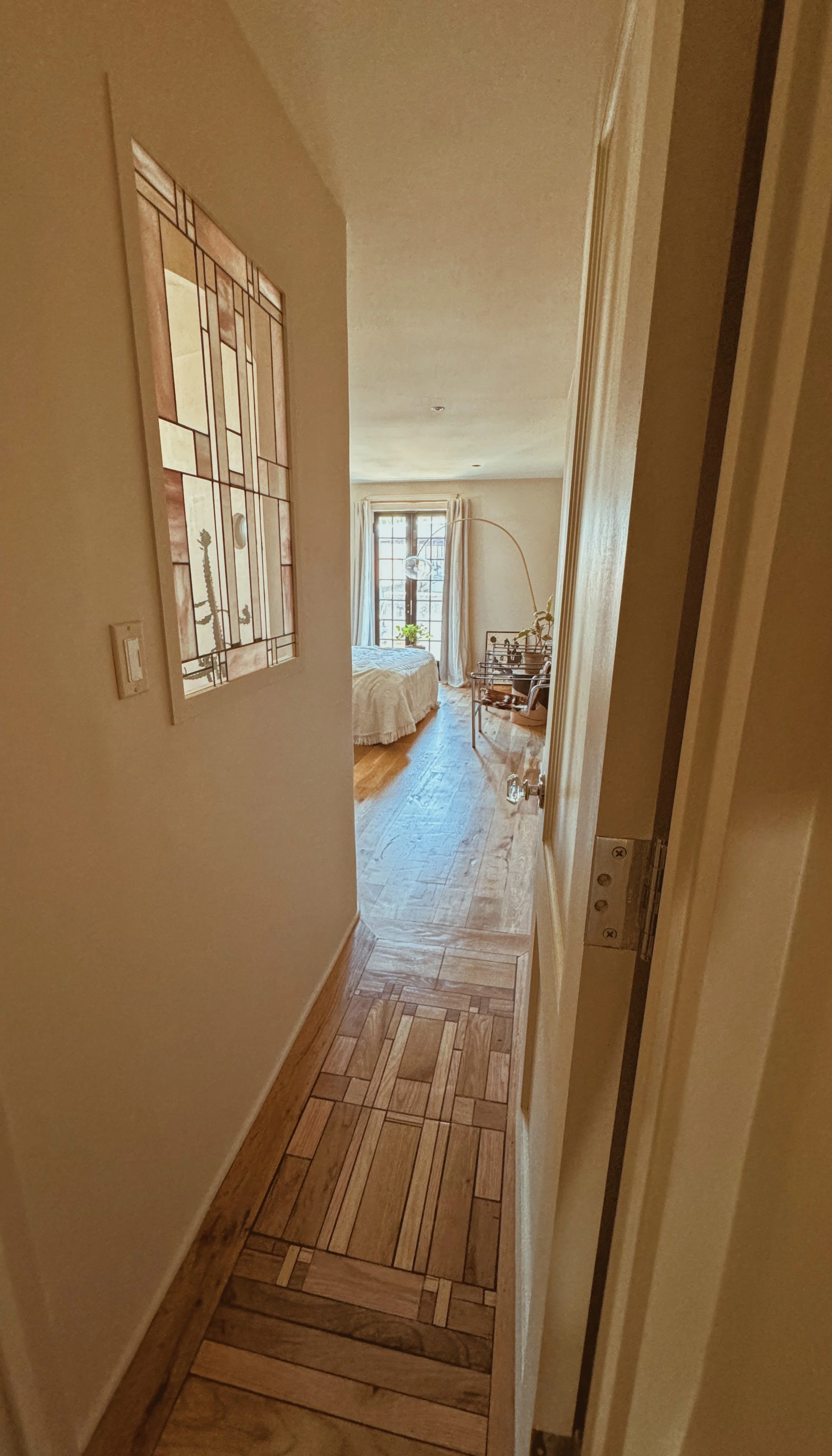 View of a hallway leading to a bedroom with a bed, large window with curtains, and a small table with chairs.